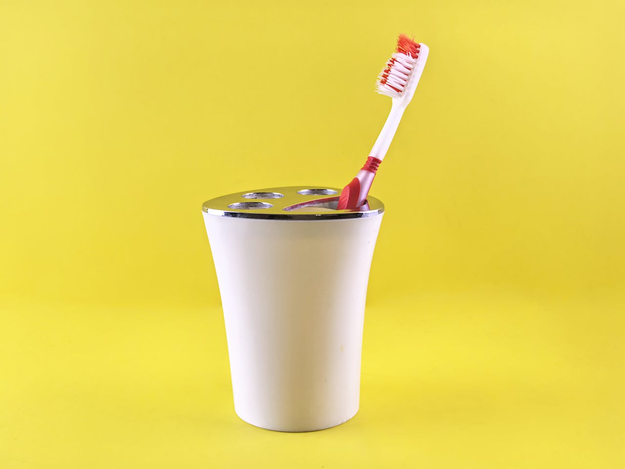 Simple white toothbrush holder with red toothbrush on vibrant yellow background.