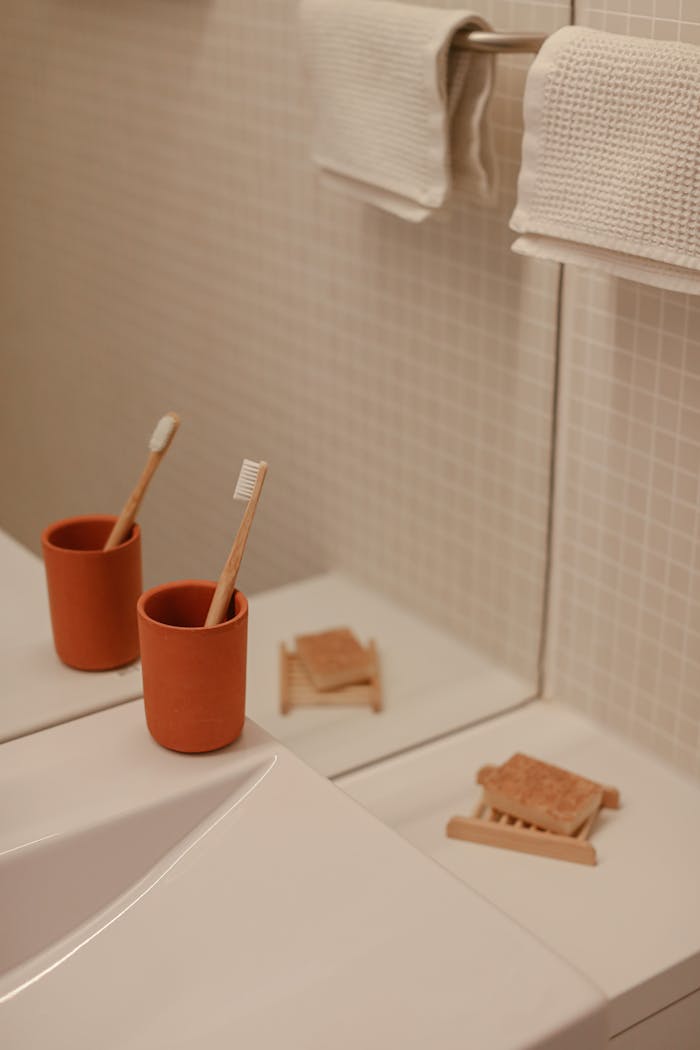 A minimalist bathroom scene featuring a bamboo toothbrush in a ceramic cup with a mirror reflection.